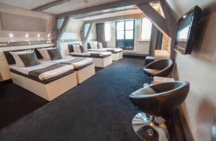 Hotel CC gay-friendly hotel room. Three beds, black carpet, chairs, and exposed beams. A comfortable space for gay travelers in Amsterdam.