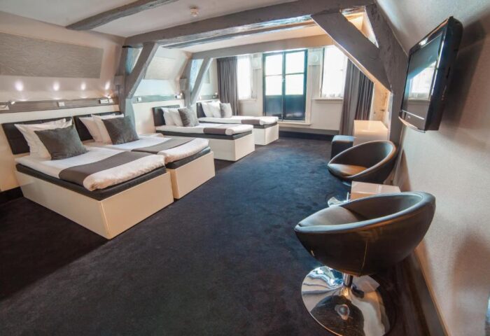 Hotel CC gay-friendly hotel room. Three beds, black carpet, chairs, and exposed beams. A comfortable space for gay travelers in Amsterdam.
