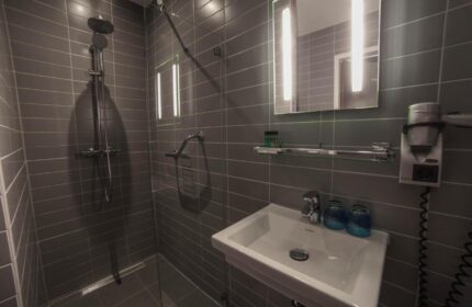 Hotel CC bathroom. Gay-friendly hotel features modern shower, sink, and mirror. Gray tile design. Ideal for gay men travel. Hotel CC offers comfort.