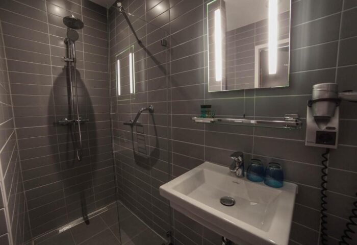 Hotel CC bathroom. Gay-friendly hotel features modern shower, sink, and mirror. Gray tile design. Ideal for gay men travel. Hotel CC offers comfort.