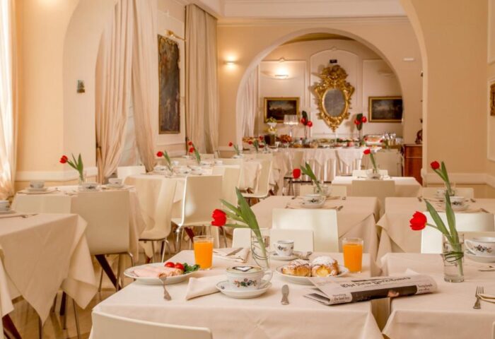 Breakfast room at Hotel Canada, a gay-friendly hotel. Tables are set with tulips, pastries, juice, and newspapers. Buffet in background.