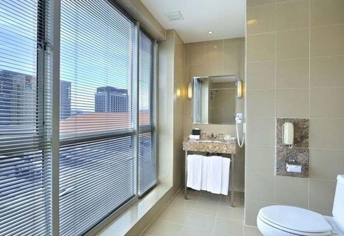 Bathroom at Gay-Friendly Hotel Capitol Kuala Lumpur: Sink, toilet, and large window with blinds offering city views. Modern design.