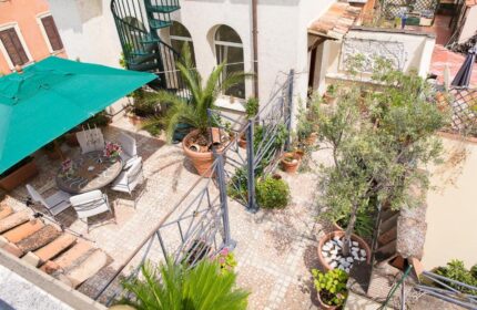 Hotel Celio's gay-friendly rooftop terrace. Outdoor seating area with umbrella, plants, and spiral staircase. Perfect for gay travelers.