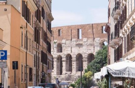 Street view of Hotel Celio, a gay-friendly hotel in Rome, Italy. The Colosseum is visible in the background. Pedestrians crossing the street.