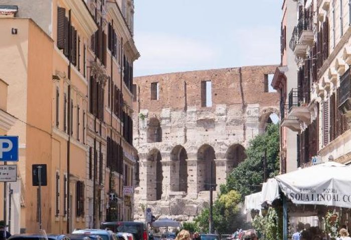 Street view of Hotel Celio, a gay-friendly hotel in Rome, Italy. The Colosseum is visible in the background. Pedestrians crossing the street.