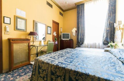 Hotel Celio room: Gay-friendly hotel room with blue floral bedspread, desk, and TV. A comfortable stay for gay travelers in Rome, Italy.