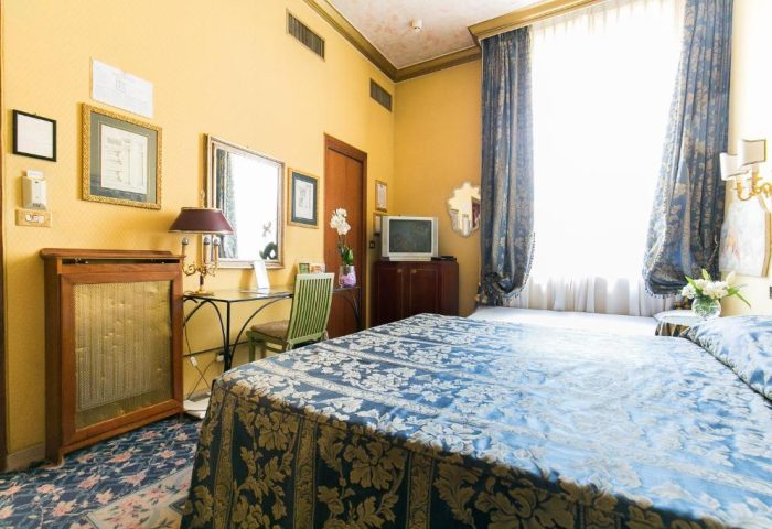 Hotel Celio room: Gay-friendly hotel room with blue floral bedspread, desk, and TV. A comfortable stay for gay travelers in Rome, Italy.