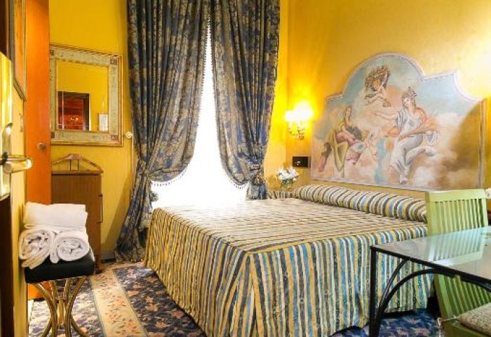 Hotel Celio gay-friendly hotel room. A double bed with a painted headboard, blue floral carpet, and yellow walls. Gay travel in Rome.