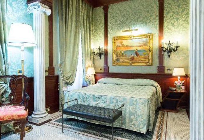 Hotel Celio gay-friendly hotel room. Luxurious suite with columns, patterned wallpaper, and mosaic tile floor. Comfortable gay travel.