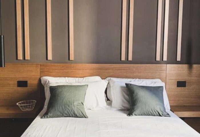 Hotel Central Lodge gay-friendly room. Modern bedroom with wooden headboard, white linens, gray pillows, and decorative wall panels.