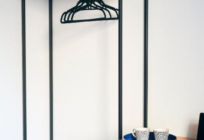 Hotel Central Lodge's gay-friendly room: minimalist closet with pillows, hangers, desk with laptop and mugs. Modern, clean design.