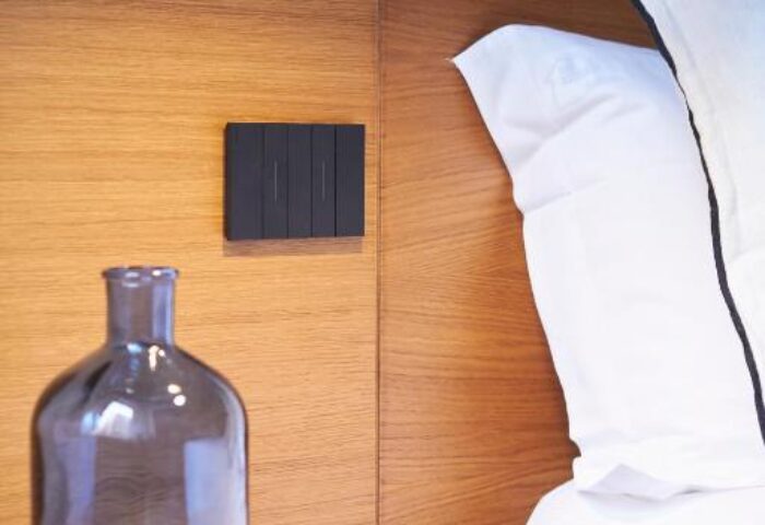 Hotel Central Lodge gay-friendly room detail. Bed with white linens, wood headboard, bedside table with blue glass bottle. Modern, stylish decor.