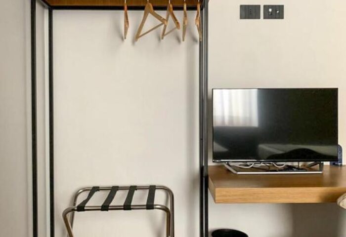 Hotel Central Lodge's gay-friendly room: closet with hangers, luggage rack, TV, desk, and stool. Perfect for gay men's travel needs.