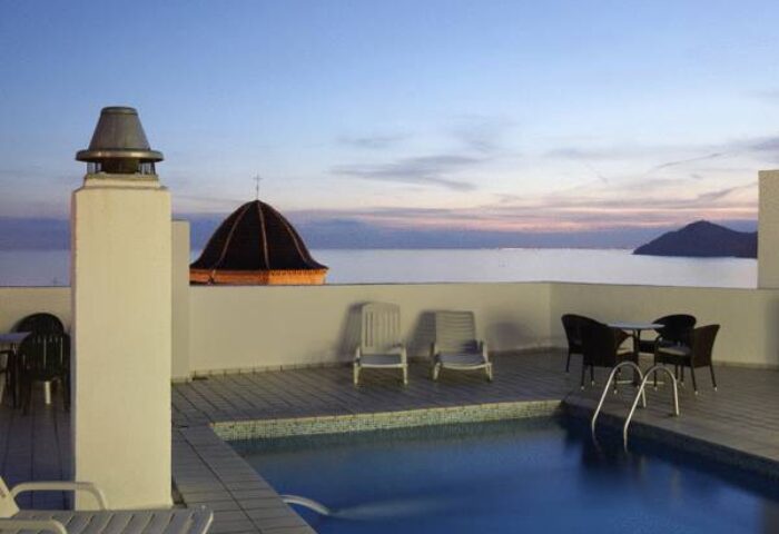 Hotel Centro Mar's rooftop pool at dusk. Gay-friendly hotel with ocean view, lounge chairs, and table. Ideal for gay travel advice seekers.