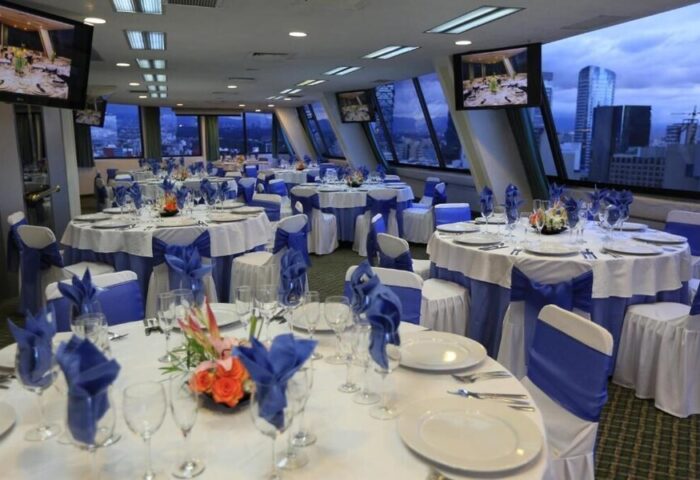 Gay-friendly Hotel Century Reforma banquet room. Tables set with white linens and blue accents, cityscape view. Ideal for events.
