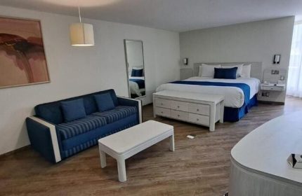 Hotel Century Reforma gay-friendly room. A king-size bed with white linens, a blue accent, and a sofa. A modern, comfortable space.