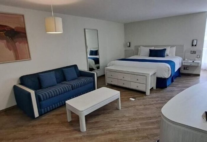 Hotel Century Reforma gay-friendly room. A king-size bed with white linens, a blue accent, and a sofa. A modern, comfortable space.