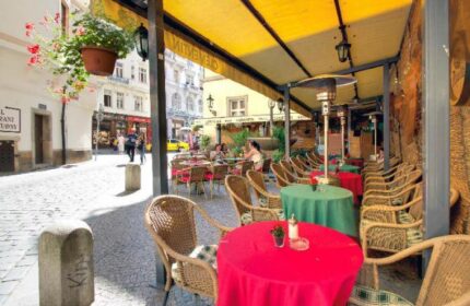 Hotel Clementin Old Town's pet-friendly, gay-friendly charm. Outdoor cafe seating with vibrant red and green tables on a cobblestone street.
