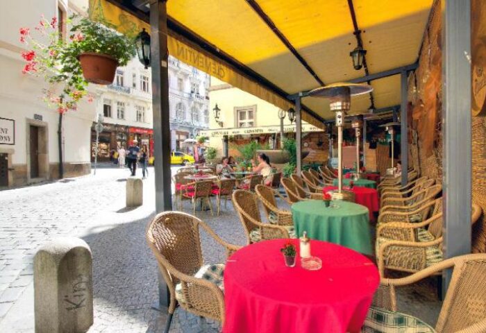 Hotel Clementin Old Town's pet-friendly, gay-friendly charm. Outdoor cafe seating with vibrant red and green tables on a cobblestone street.