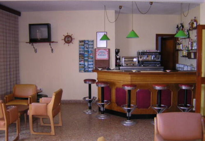 Hotel Condestable's bar area, a gay-friendly hotel. Stools line the bar, with seating nearby. A TV is on the wall.