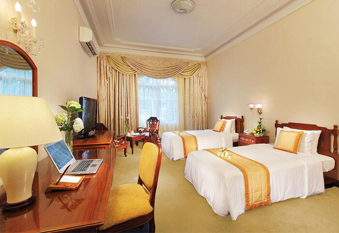 Hotel Continental Saigon room with two beds. Gay-friendly hotel featuring a desk, TV, and elegant decor for a comfortable stay.