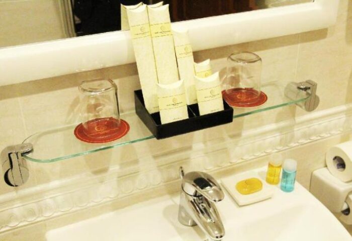 Hotel Continental Saigon's bathroom sink and amenities. Gay-friendly hotel with soap, shampoo, and glasses on a glass shelf.