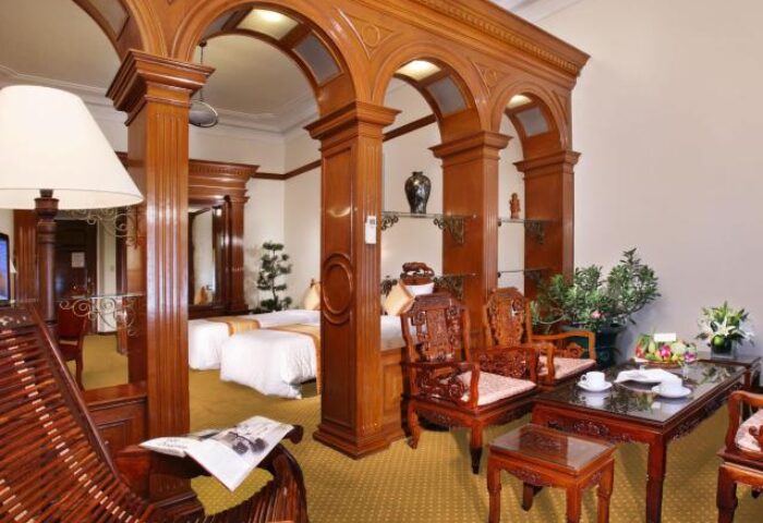 Hotel Continental Saigon room with wooden arches. Gay-friendly hotel interior with chairs, table, and beds. Saigon travel for gay men.