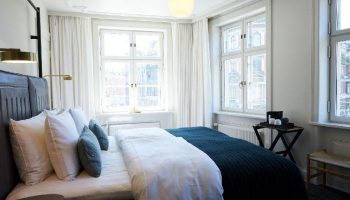 Gay-Friendly Hotel Danmark by Brøchner Hotels bedroom. Interior of a stylish room with bed, pillows, lamps, windows, and bedside table.