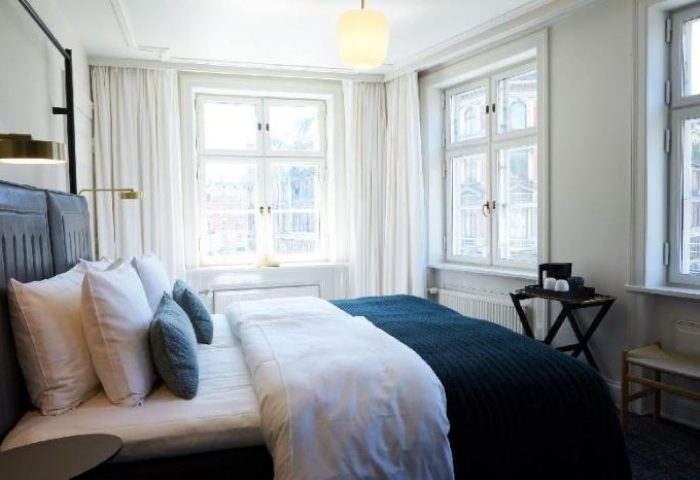 Gay-Friendly Hotel Danmark by Brøchner Hotels bedroom. Interior of a stylish room with bed, pillows, lamps, windows, and bedside table.