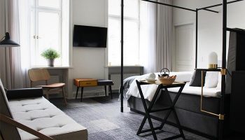 Hotel Danmark by Brøchner Hotels room interior. Gay-friendly hotel with four-poster bed, sofa, and modern design. Travel destination for gay men.