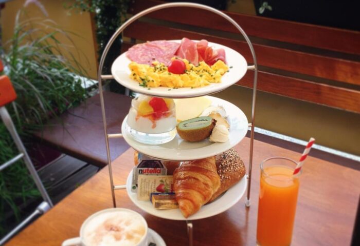 Gay-friendly Hotel Deutsche Eiche breakfast tower with meats, eggs, fruit, pastries, juice, and coffee. Delicious start to your Munich stay.