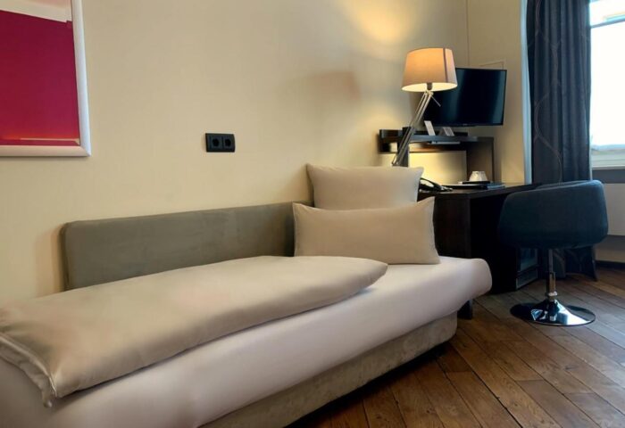 Hotel Deutsche Eiche gay-friendly room. Couch with pillows, desk, chair, TV, and lamp. Gay travel lodging in Munich.