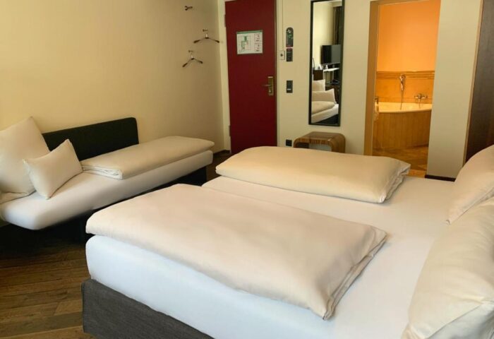 Hotel Deutsche Eiche gay-friendly room. Beds, couch, red door, and bathroom with tub. Gay travel lodging in Munich, Germany.