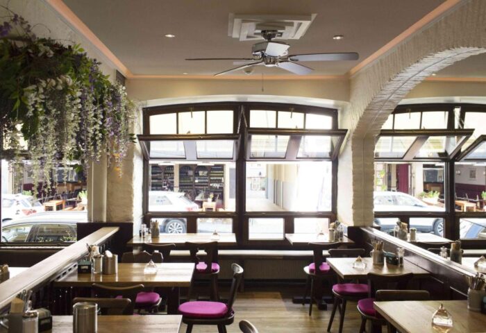 Hotel Deutsche Eiche's gay-friendly interior. The Munich hotel features a dining area with large windows, wood tables, and purple chairs.