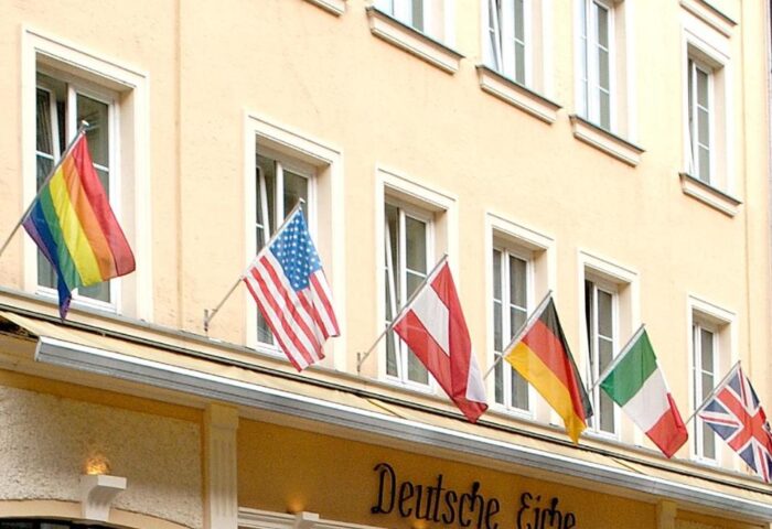 Hotel Deutsche Eiche facade. Gay-friendly hotel with rainbow flag and international flags. Popular gay travel destination in Munich, Germany.