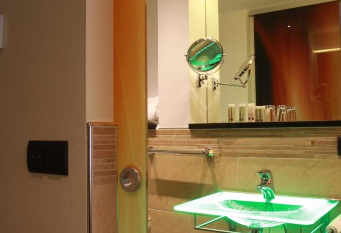 Hotel Deutsche Eiche's gay-friendly bathroom. Features a modern glass sink with green lighting, a sleek mirror, and tiled walls.