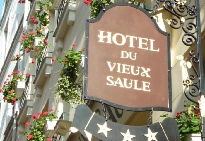 Hotel Du Vieux Saule, a gay-friendly, pet-friendly hotel. Facade with flower boxes and a sign with the hotel's name and star rating.
