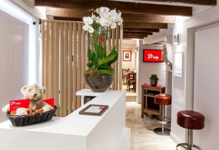 Hotel Dwin's lobby. Gay-friendly, pet-friendly hotel. White reception desk, orchids, teddy bear, and view to the restaurant. Beams on the ceiling.