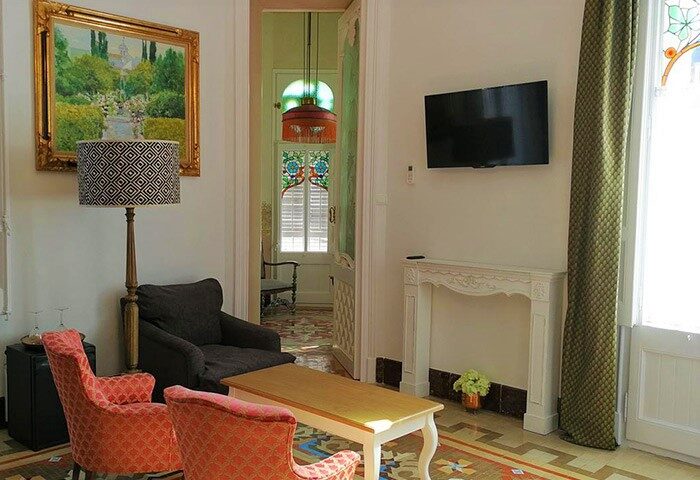 Hotel El Xalet gay-friendly hotel room. Interior view with chairs, table, TV, and doorway. A welcoming space for gay travelers.