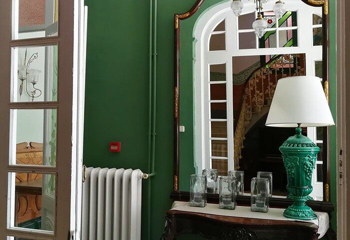 Hotel El Xalet interior. Gay-friendly hotel with green walls, vintage furniture, and a mirror reflecting the staircase. Stylish gay travel lodging.