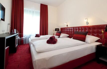Hotel Esplanade Köln gay-friendly room. Two beds with red accents, desk, and TV. Modern design for gay men travelers in Cologne.