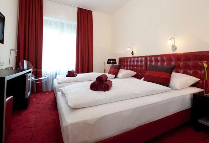 Hotel Esplanade Köln gay-friendly room. Two beds with red accents, desk, and TV. Modern design for gay men travelers in Cologne.