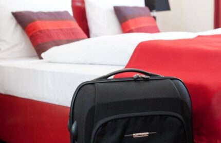 Hotel Esplanade Köln room. Gay-friendly hotel room with red decor. Suitcase in front of a bed with white sheets, red blanket, and pillows.