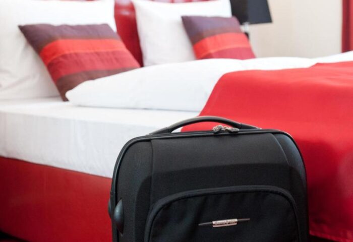 Hotel Esplanade Köln room. Gay-friendly hotel room with red decor. Suitcase in front of a bed with white sheets, red blanket, and pillows.