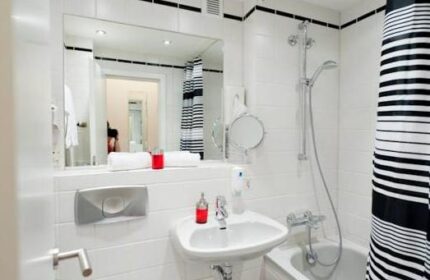 Bathroom at Hotel Esplanade Köln, a gay-friendly hotel. Features white tiles, sink, tub with shower, mirror, and black and white striped shower curtain.