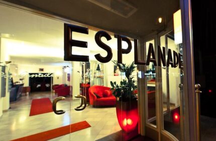Hotel Esplanade Köln entrance. Gay-friendly hotel lobby view through glass doors. Red sofas, carpets, and plant pot. Modern interior design.