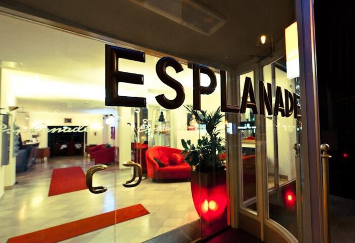 Hotel Esplanade Köln entrance. Gay-friendly hotel lobby view through glass doors. Red sofas, carpets, and plant pot. Modern interior design.