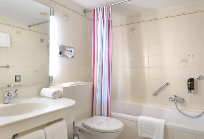 Bathroom at Hotel Europäischer Hof, a gay-friendly hotel. Features a sink, toilet, bathtub with shower curtain, and tiled walls.