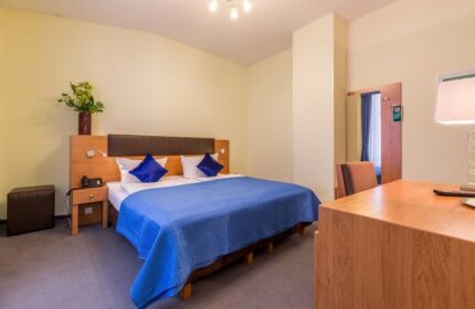 Hotel Expo Frankfurt City Centre: A gay-friendly hotel room featuring a double bed with blue cover, a desk, and a nightstand.
