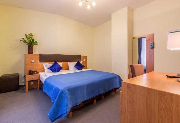 Hotel Expo Frankfurt City Centre: A gay-friendly hotel room featuring a double bed with blue cover, a desk, and a nightstand.
